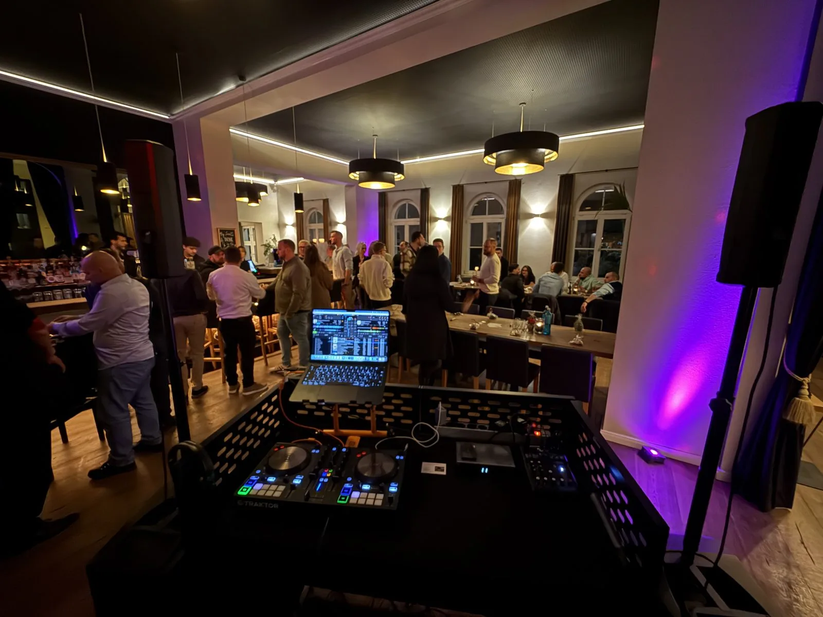 DJ Borris am DJ-Pult bei einer Firmenfeier, Gäste im Hintergrund an der Bar