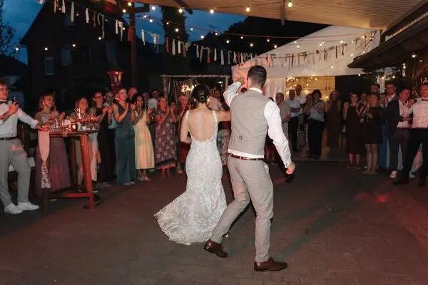 Brautpaar beim Hochzeitstanz unter Lichterkette, umringt von applaudierenden Gästen